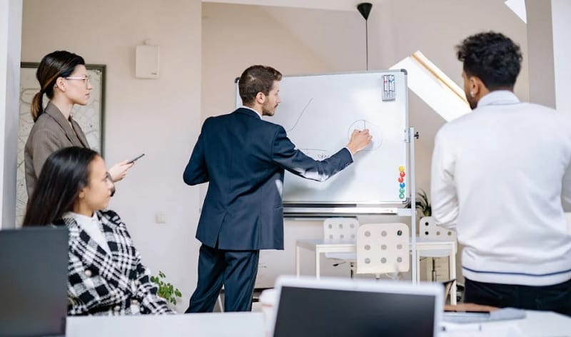 A marketing team leader standing at a whiteboard with sticky notes discussing bottom-of-the-funnel marketing.